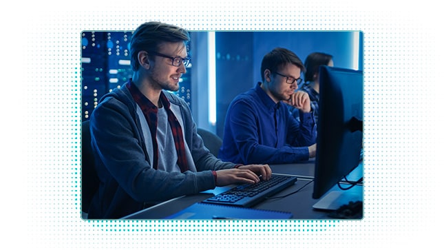 Man working on laptop, dark room lit up with blue light in background