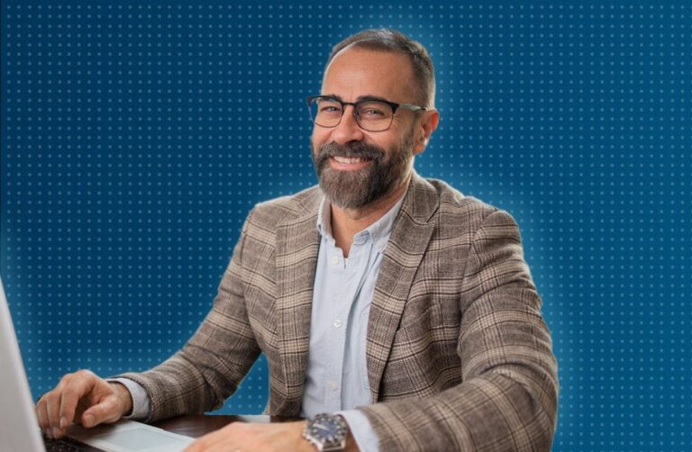 Man smiling at camera, working on desktop computer