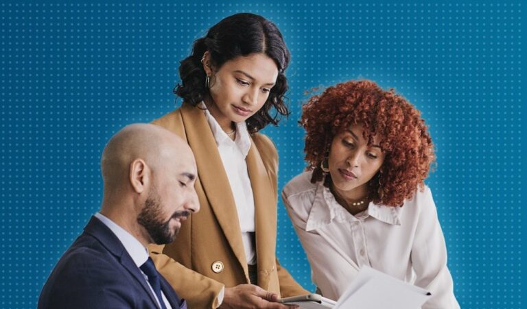 Man sitting at desk, two women looking down at desk